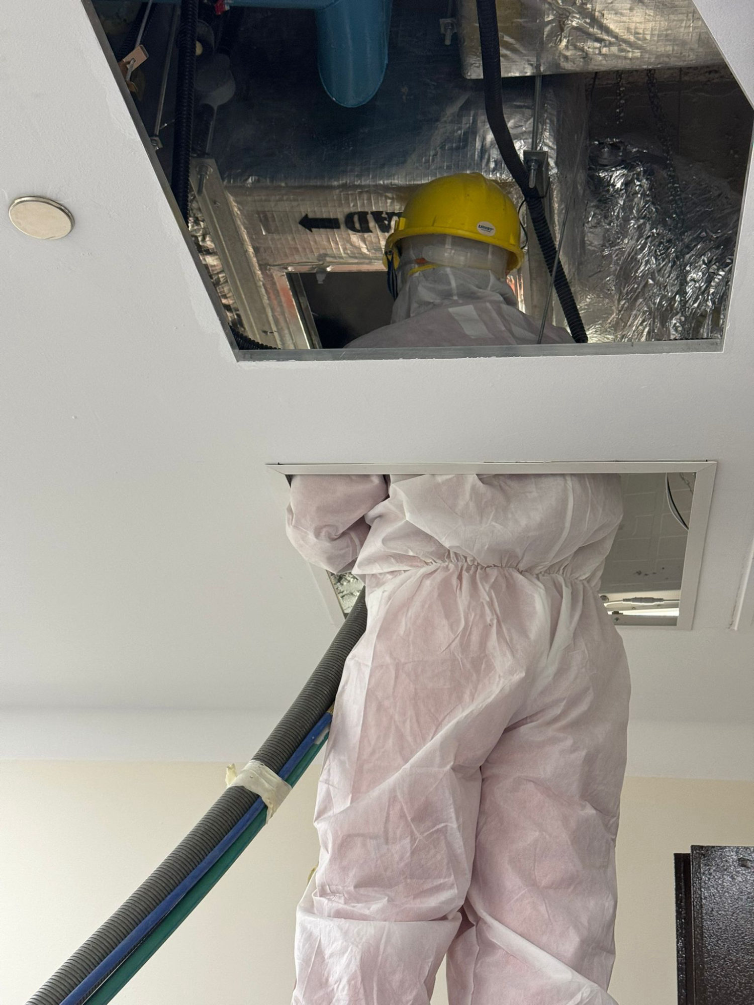 HVAC technician in protective gear inspecting a commercial air handling unit during a duct cleaning service