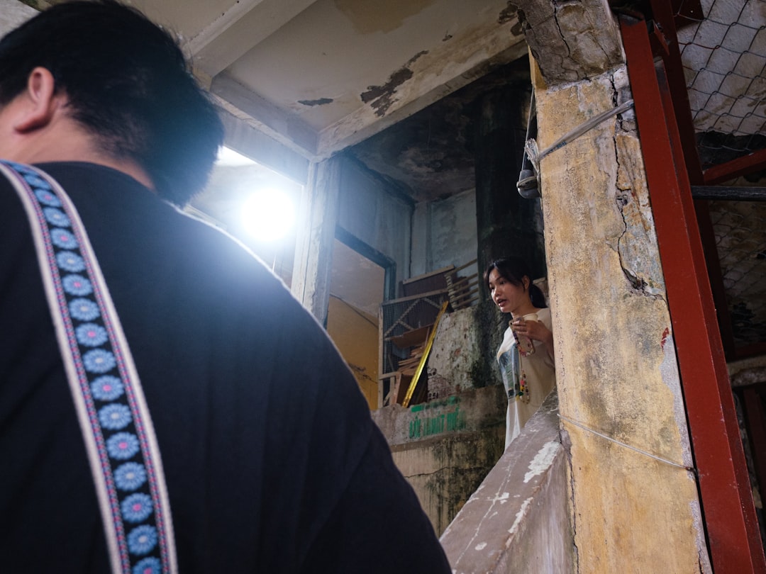 Person's back, woman in white dress peeking from doorway.
